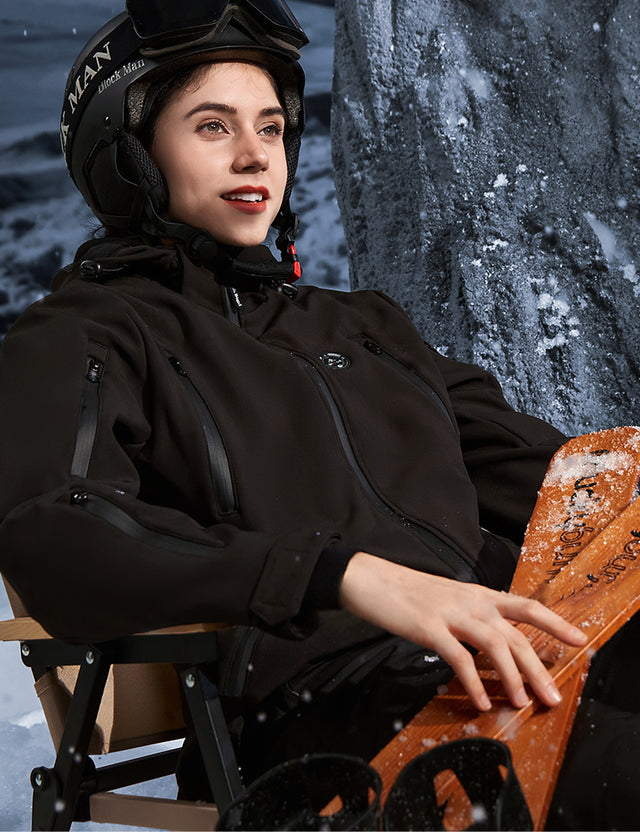 Model wearing a black heated jacket while skiing outdoors, showcasing its functionality in action.
